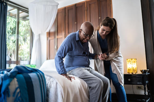 Home caregiver helping a senior Black man rise from sitting.